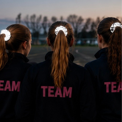 Three girls wearing jackets saying 'TEAM' all have long hair in a ponytail with a BlisSKraft reflective scrunchie.