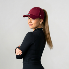 Woman wearing a Versatail Berry Red cap and black outfit against a light gray background