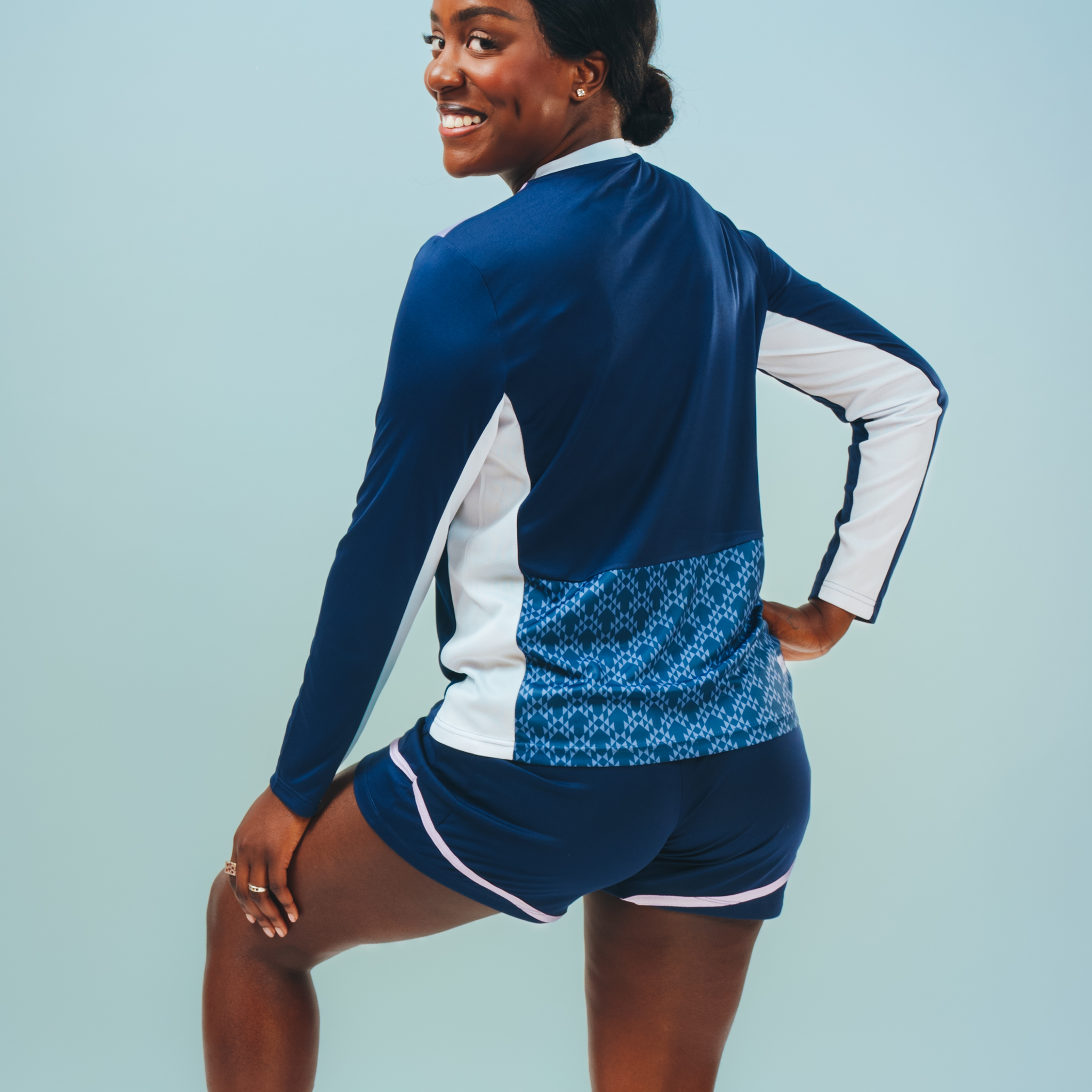 The behind view of long sleeve training top in blue with white panels and a patterned panel on the back with different shades of blue.  The training shorts are visible too with white traim.  